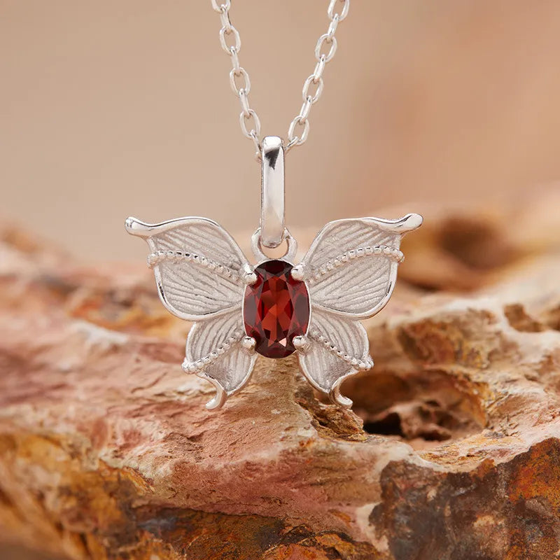 Natural Garnet gemstone butterfly necklace displayed on a rock background