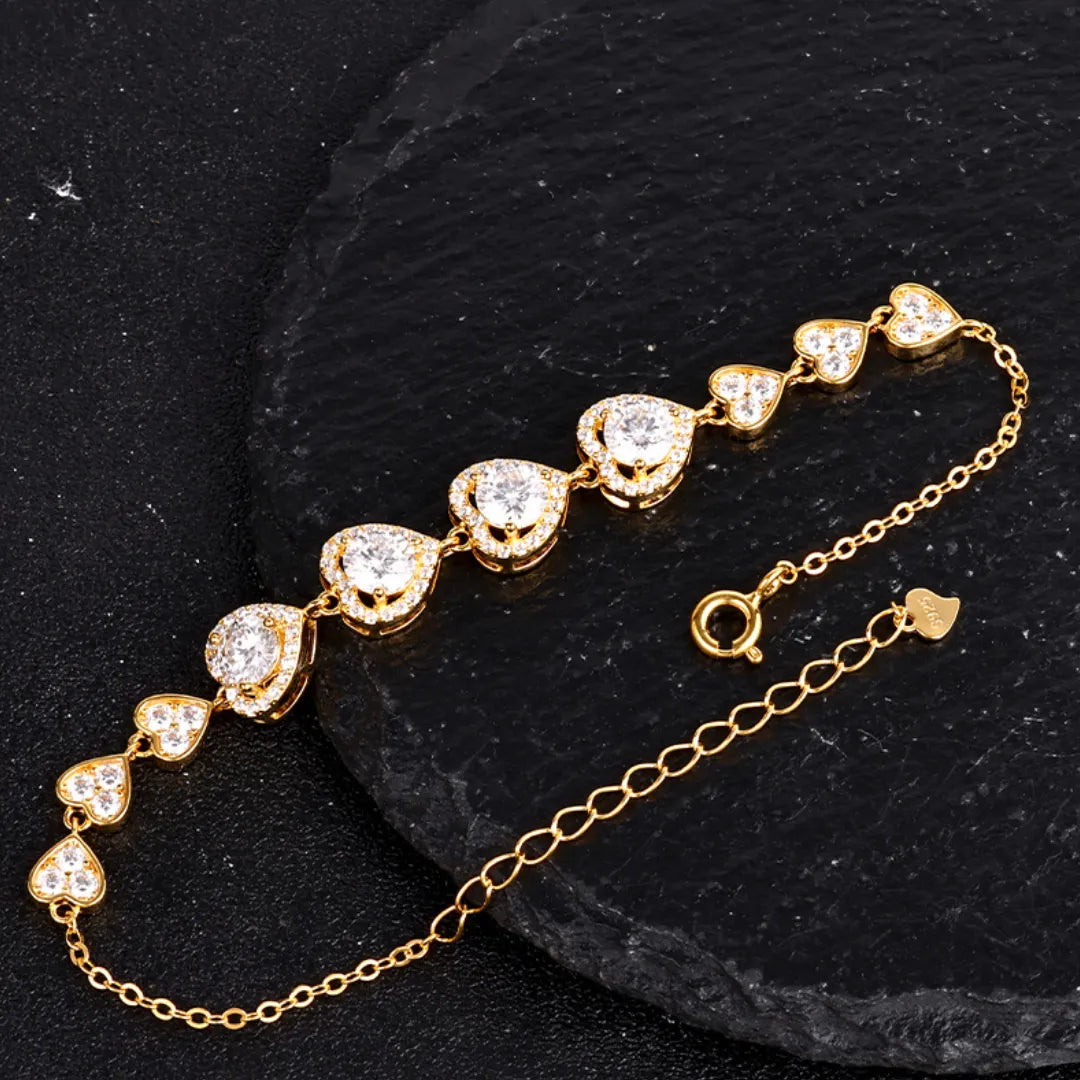 Gold-tone heart link bracelet with ten hearts set with round moissanite stones on a black textured background