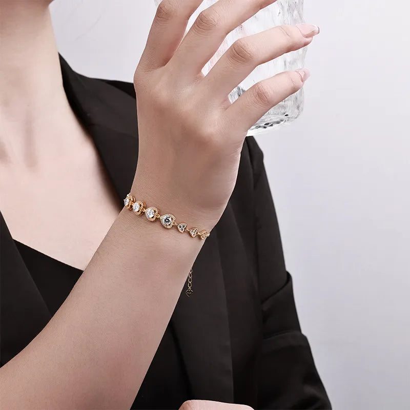 Gold-tone heart link bracelet worn on the wrist while holding a glass