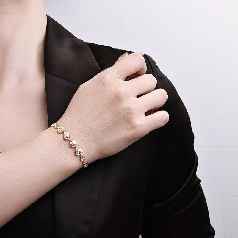Gold-tone moissanite heart bracelet worn on the wrist against a black blazer