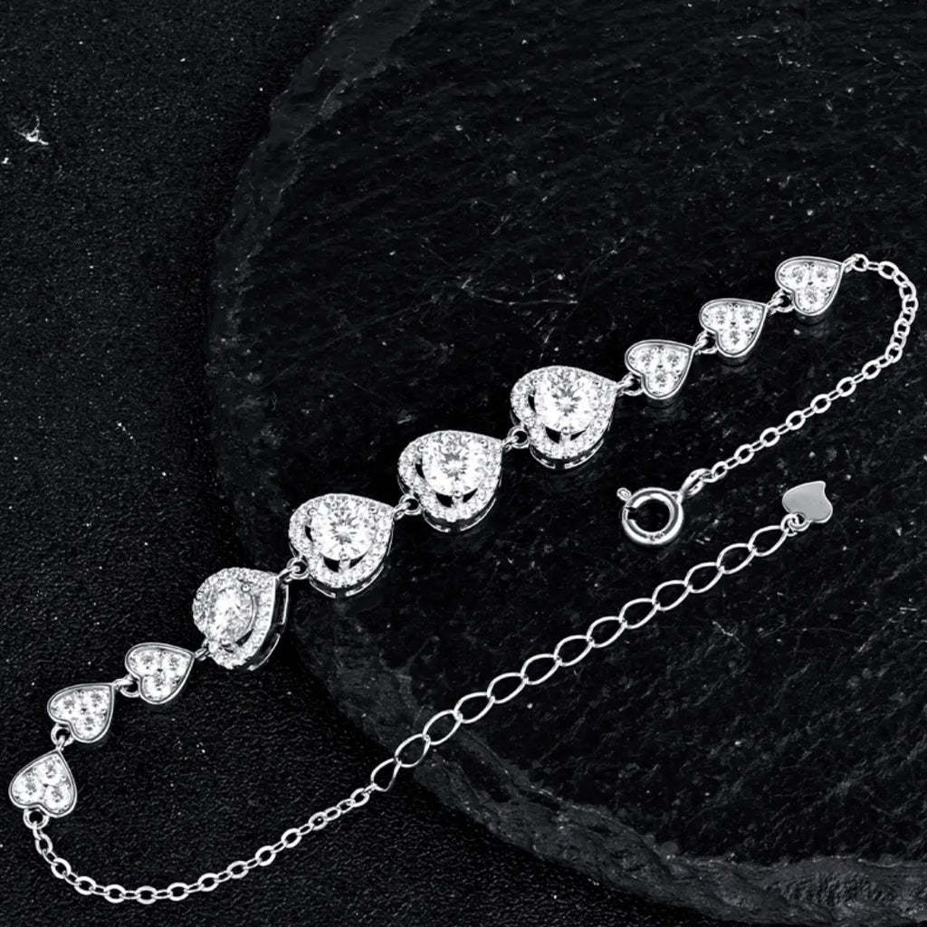 Silver heart link bracelet with a spring ring clasp and extender chain on a black textured background